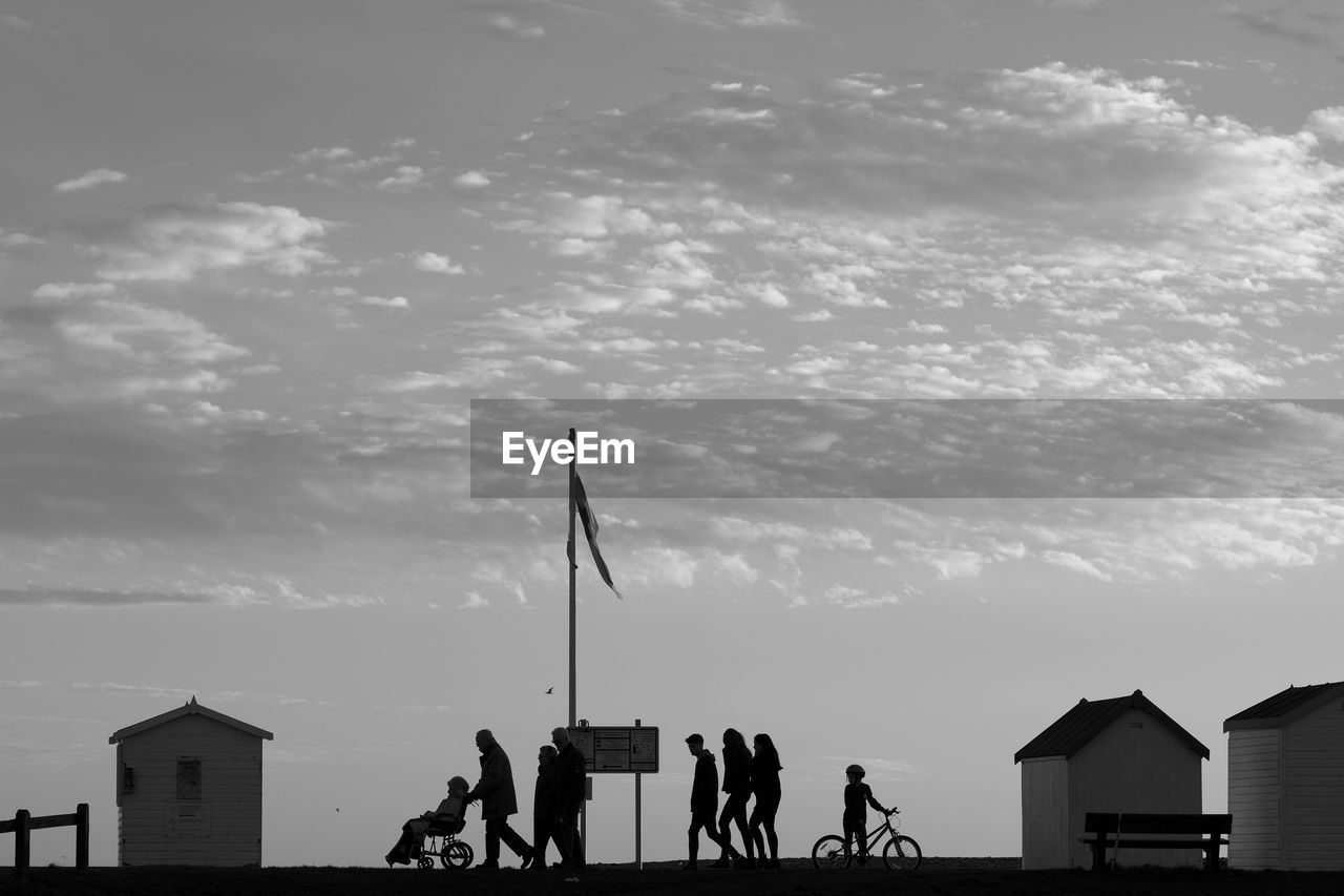 Silhouette people walking on street against cloudy sky