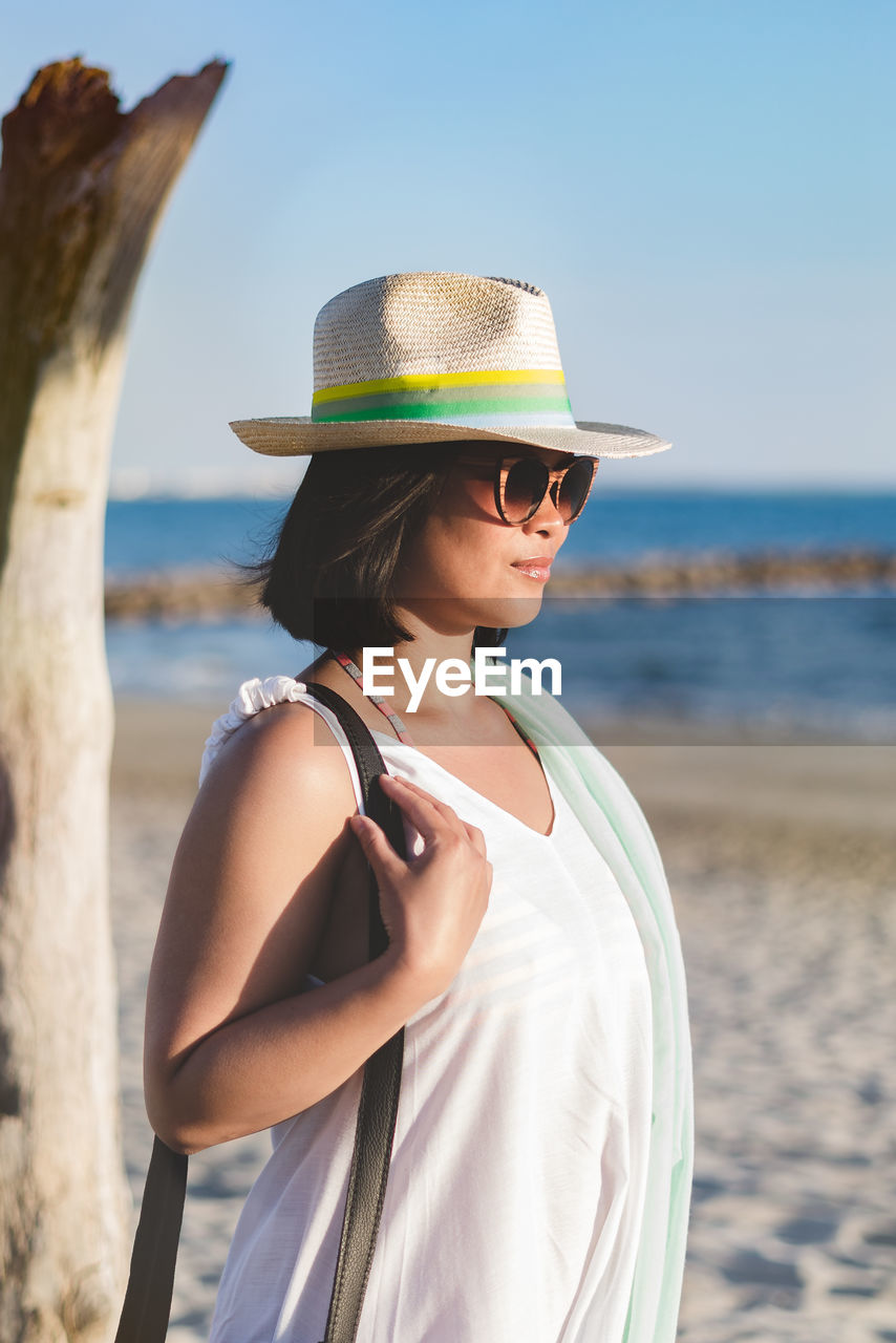 Woman wearing hat while standing at beach against clear sky