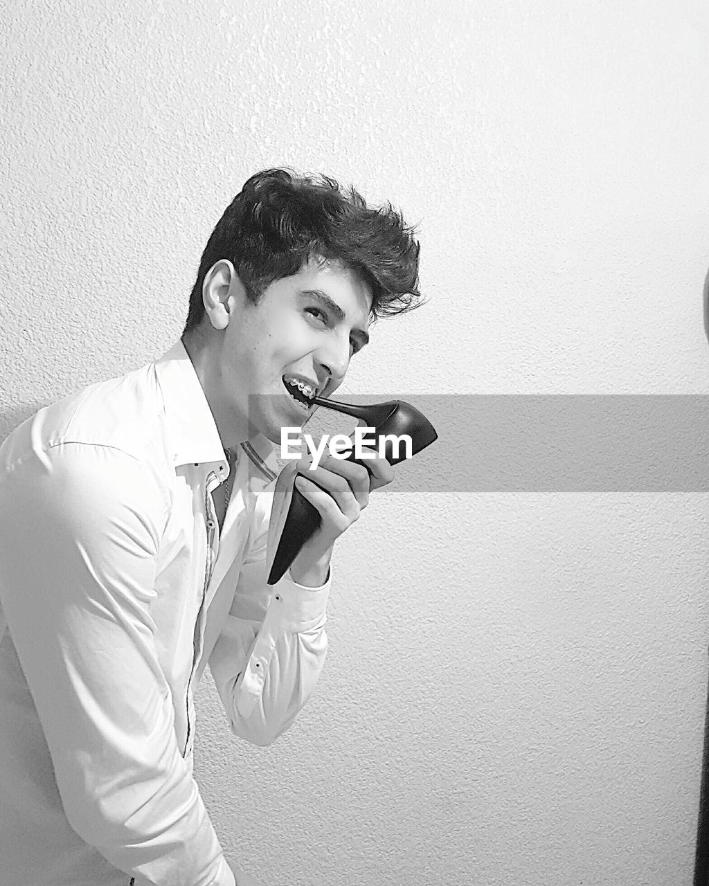 Young man with stiletto in mouth standing against white wall