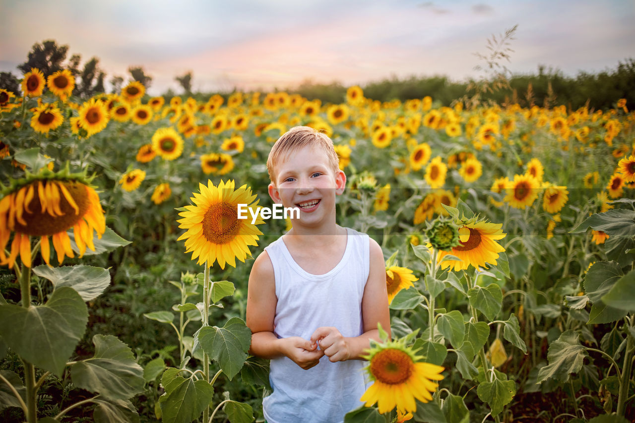 PORTRAIT OF SMILING GIRL ON SUNFLOWER FIELD AGAINST SKY