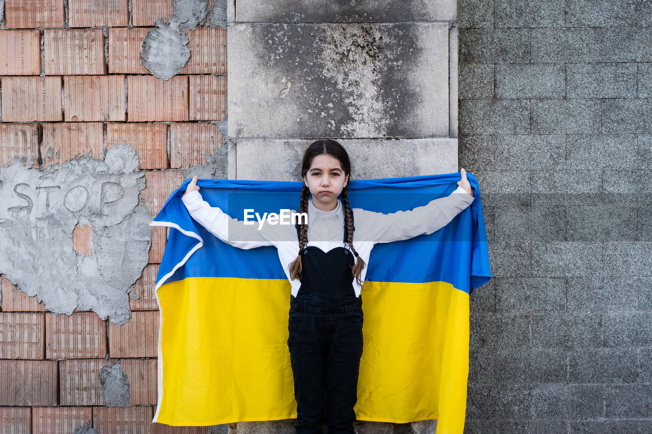 Portrait of girl holding ukrainian flag against wall