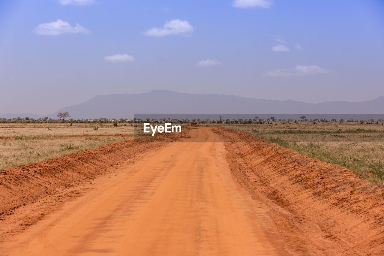 Dirt road amidst field against sky
