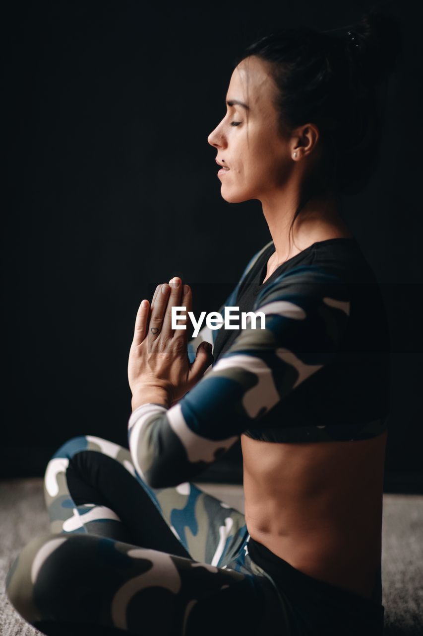 Side view of woman doing yoga while sitting at home