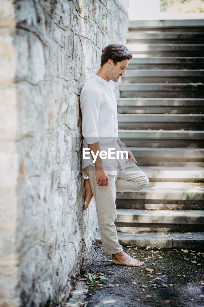 Side view of young man standing on tree trunk