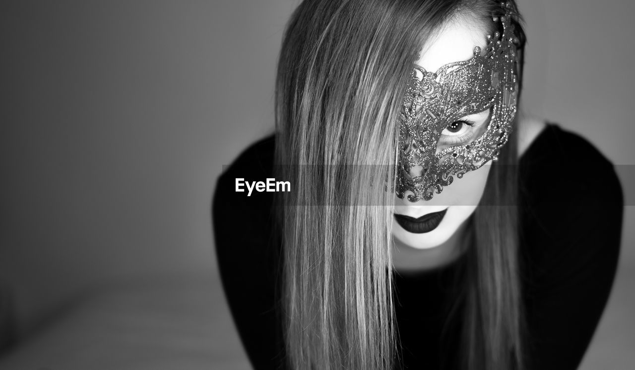 Close-up portrait of young woman wearing mask while standing against wall