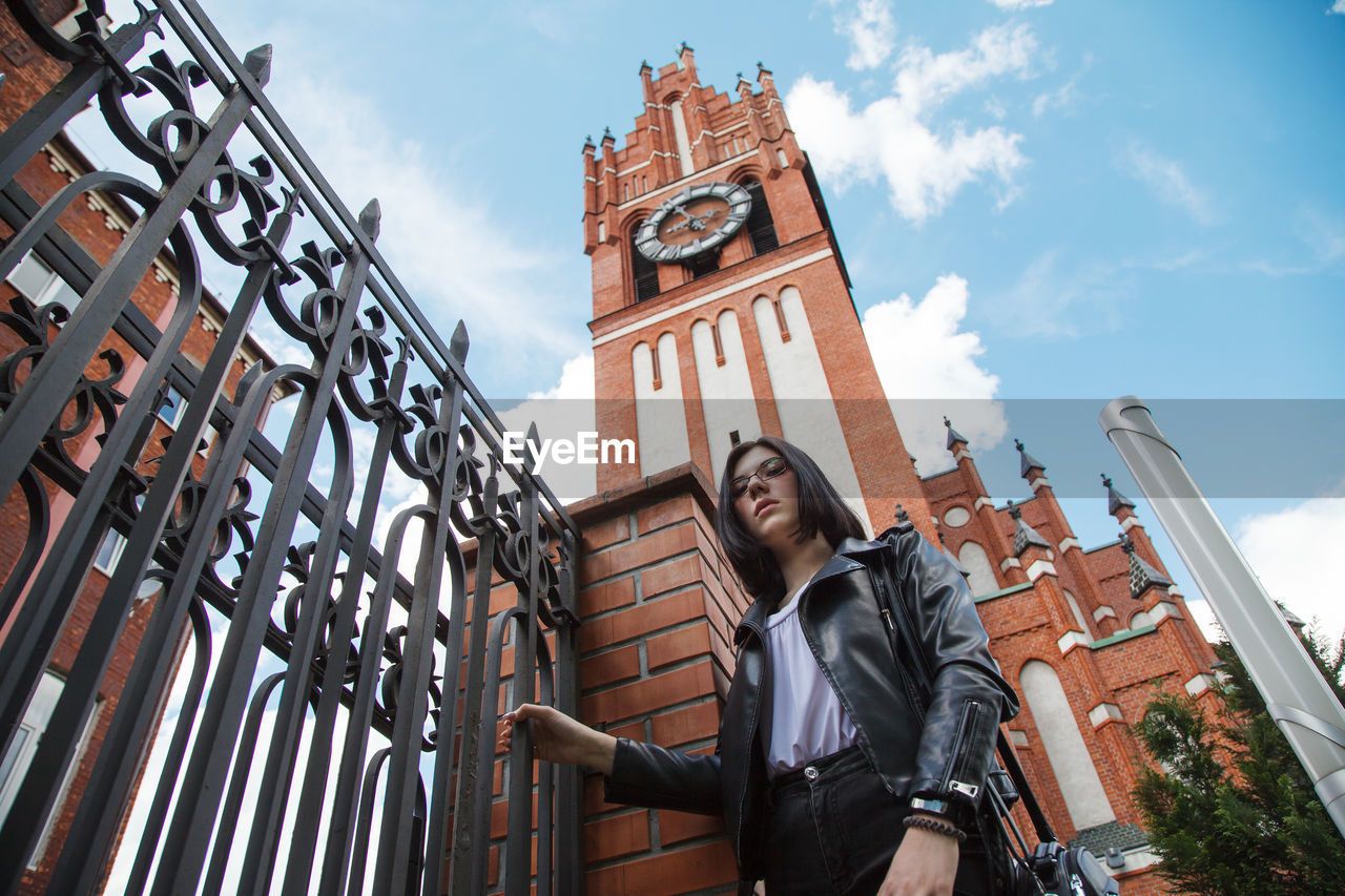 LOW ANGLE VIEW OF YOUNG WOMAN STANDING AGAINST BUILDINGS