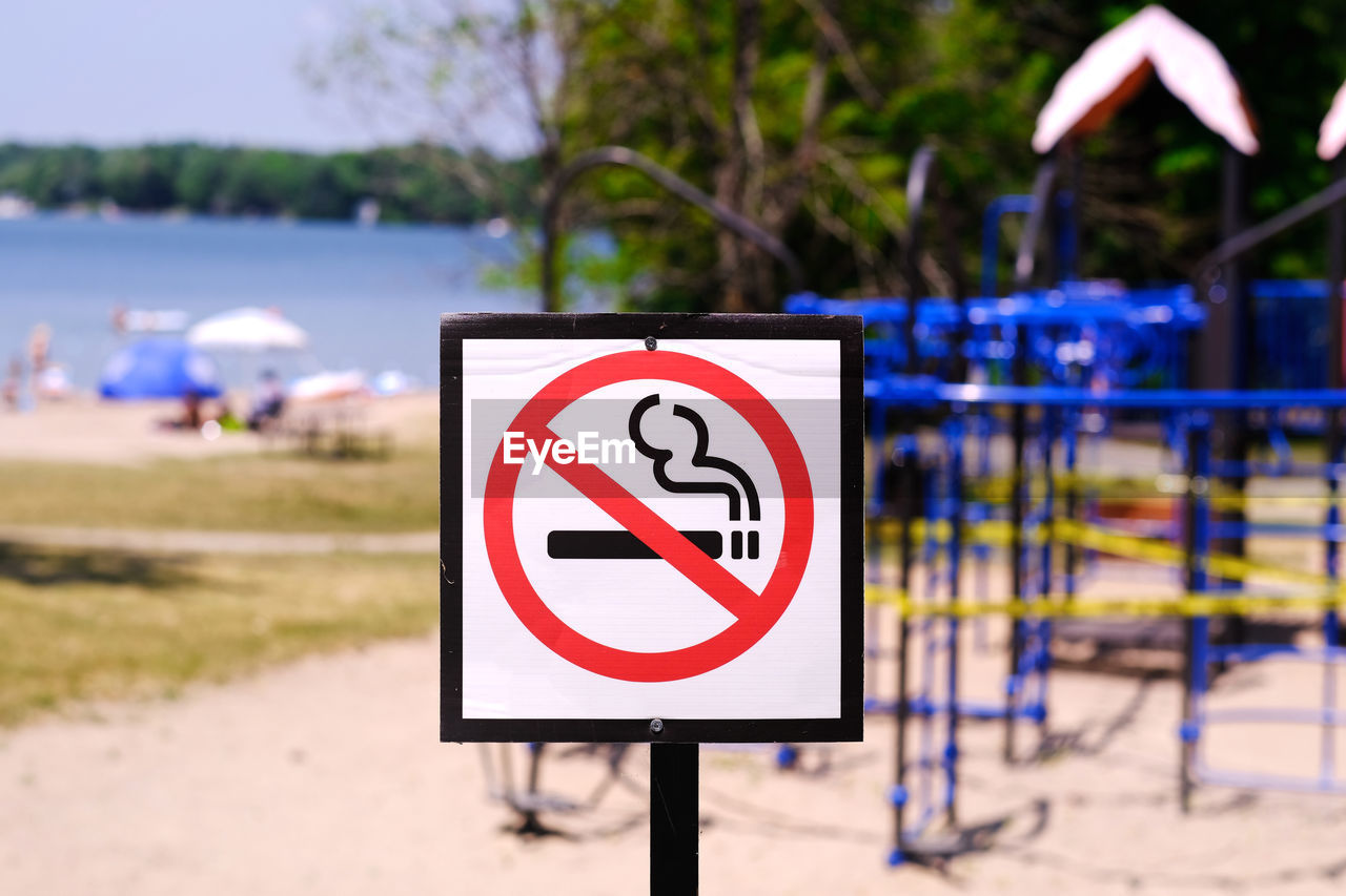 Close-up of no smoking warning sign near playground on park beside beach