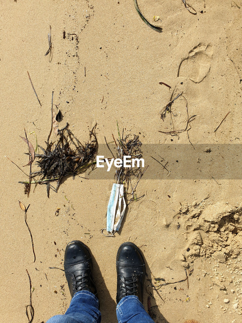 LOW SECTION OF PERSON WEARING SHOES STANDING ON SAND