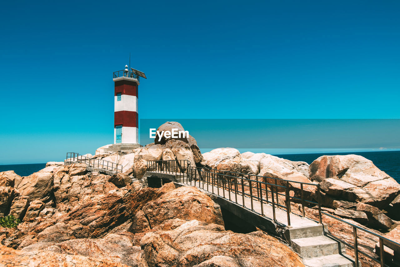 Lighthouse by sea against clear blue sky