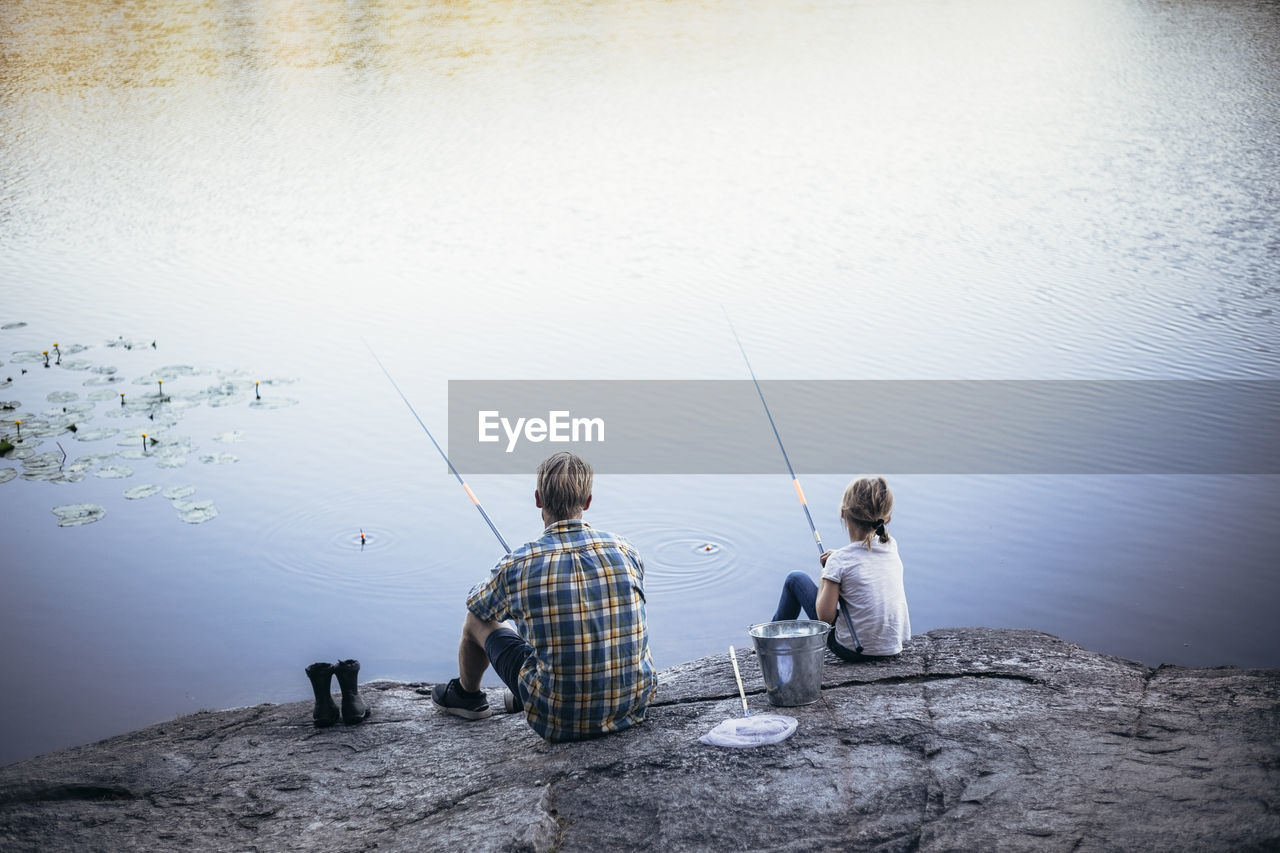 Rear view of father and daughter fishing at lake