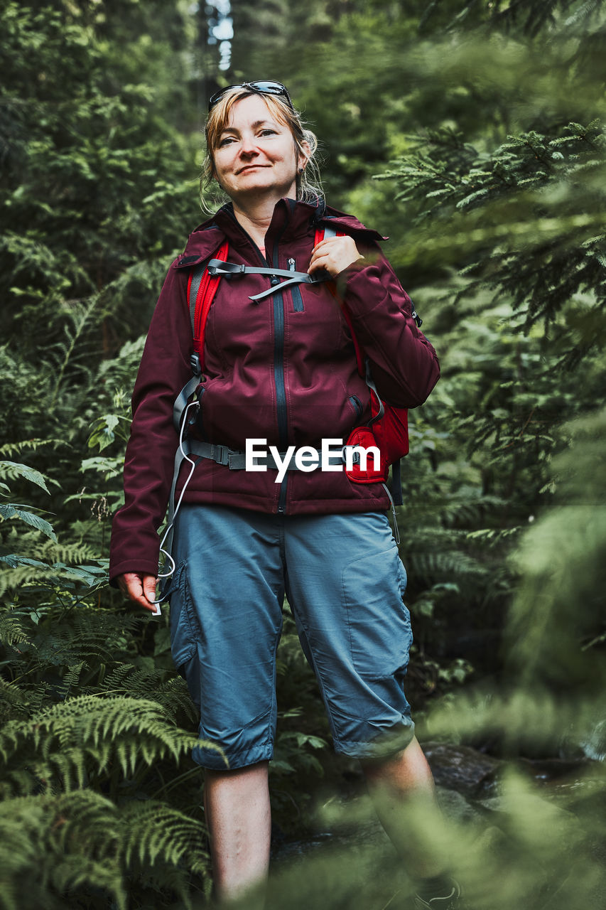 Woman with backpack hiking in forest, actively spending summer vacation close to nature