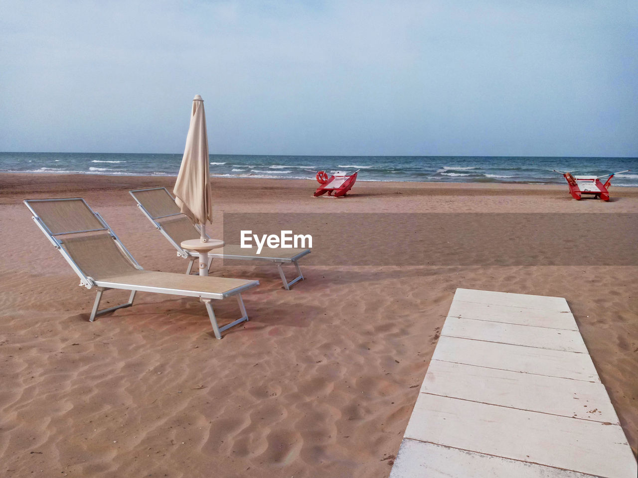 LOUNGE CHAIRS ON BEACH AGAINST SKY