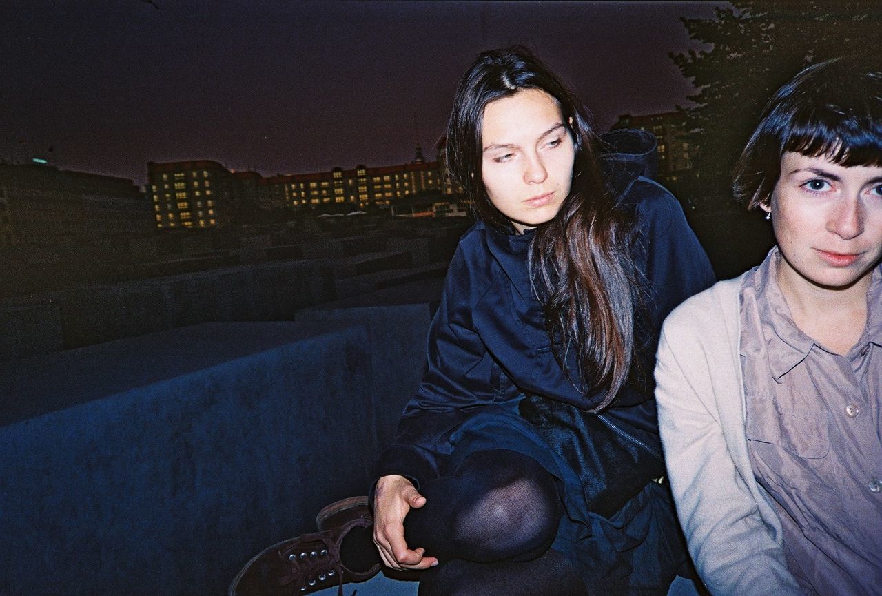 Female friends sitting on building terrace against sky at night