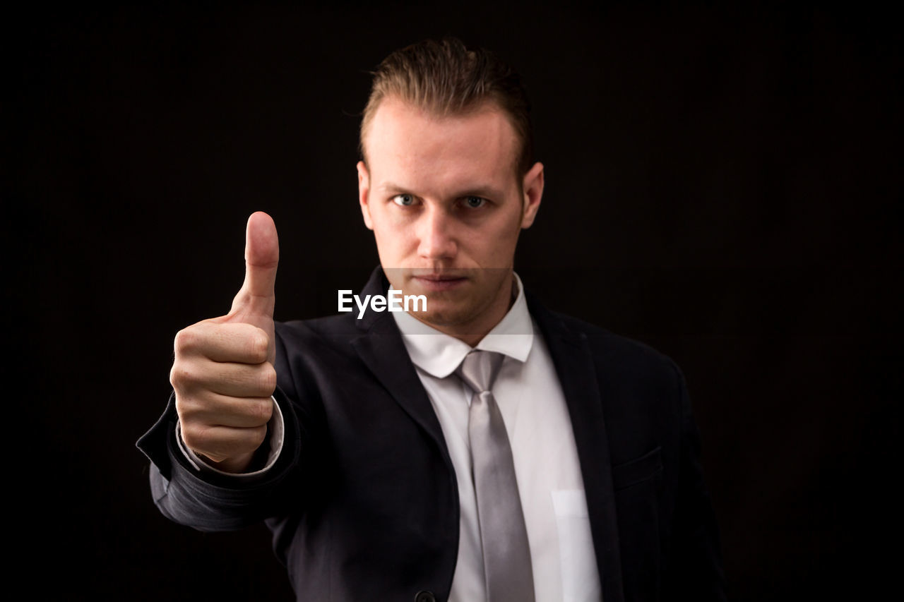 Portrait of confident businessman gesturing thumbs up against black background