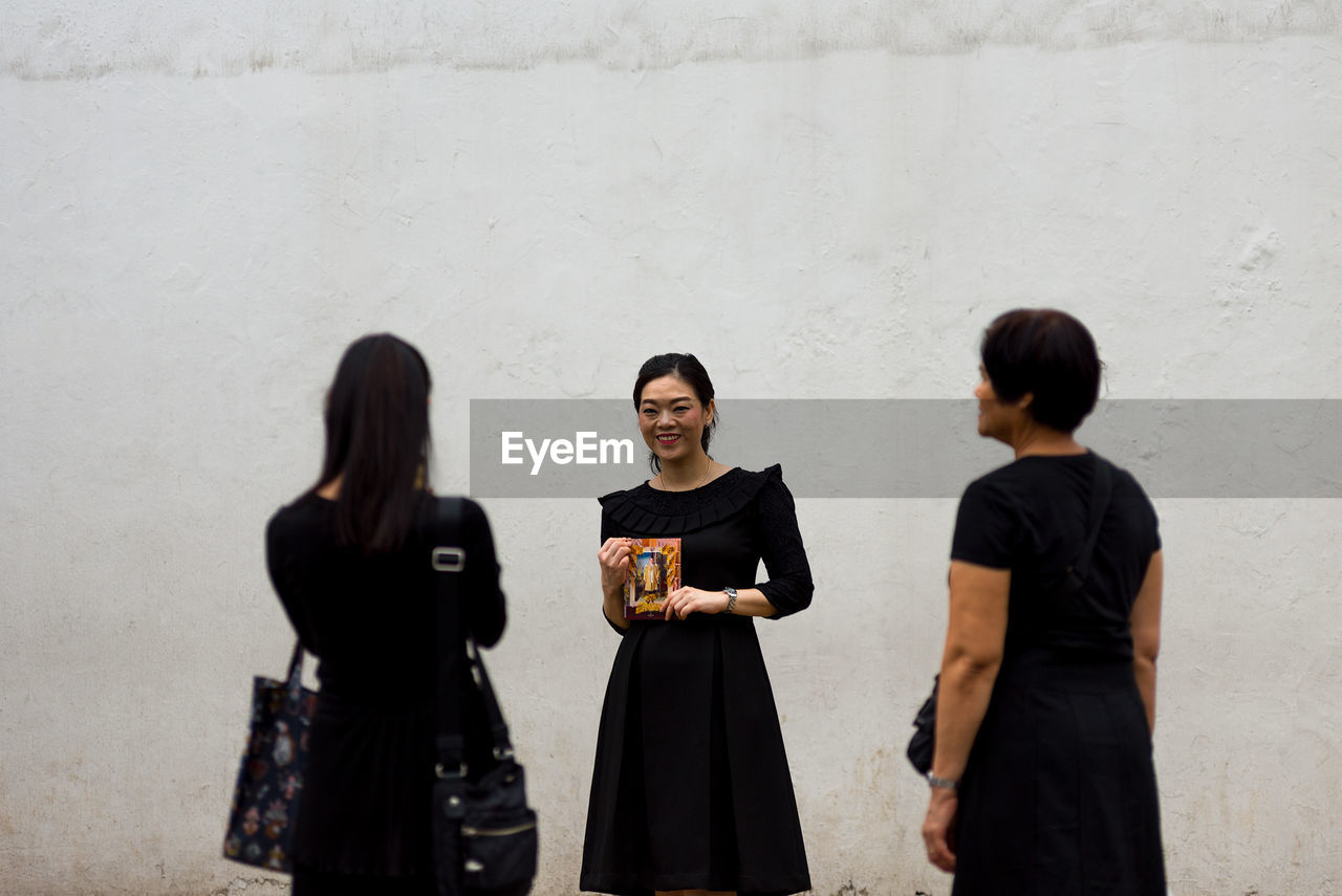 SMILING YOUNG WOMAN STANDING AGAINST WALL IN BUILDING