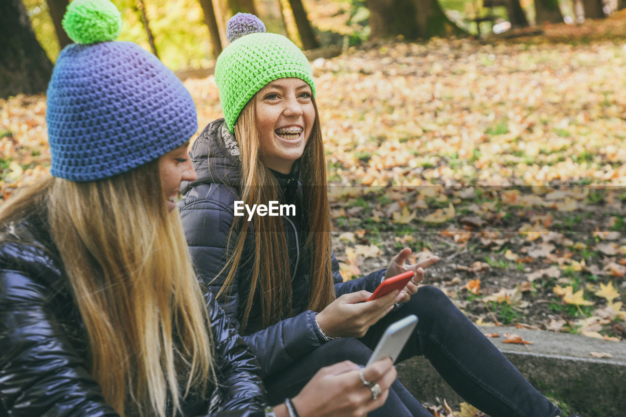 Smiling girls sitting in the park using smartphone. teen using mobile phone sisters chat with friend