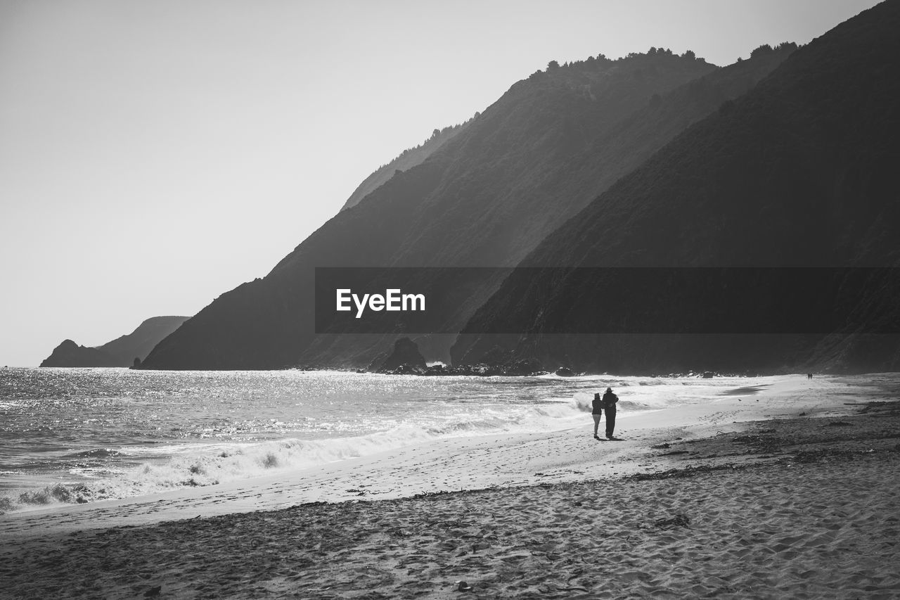 Rear view of man and woman walking at sandy beach