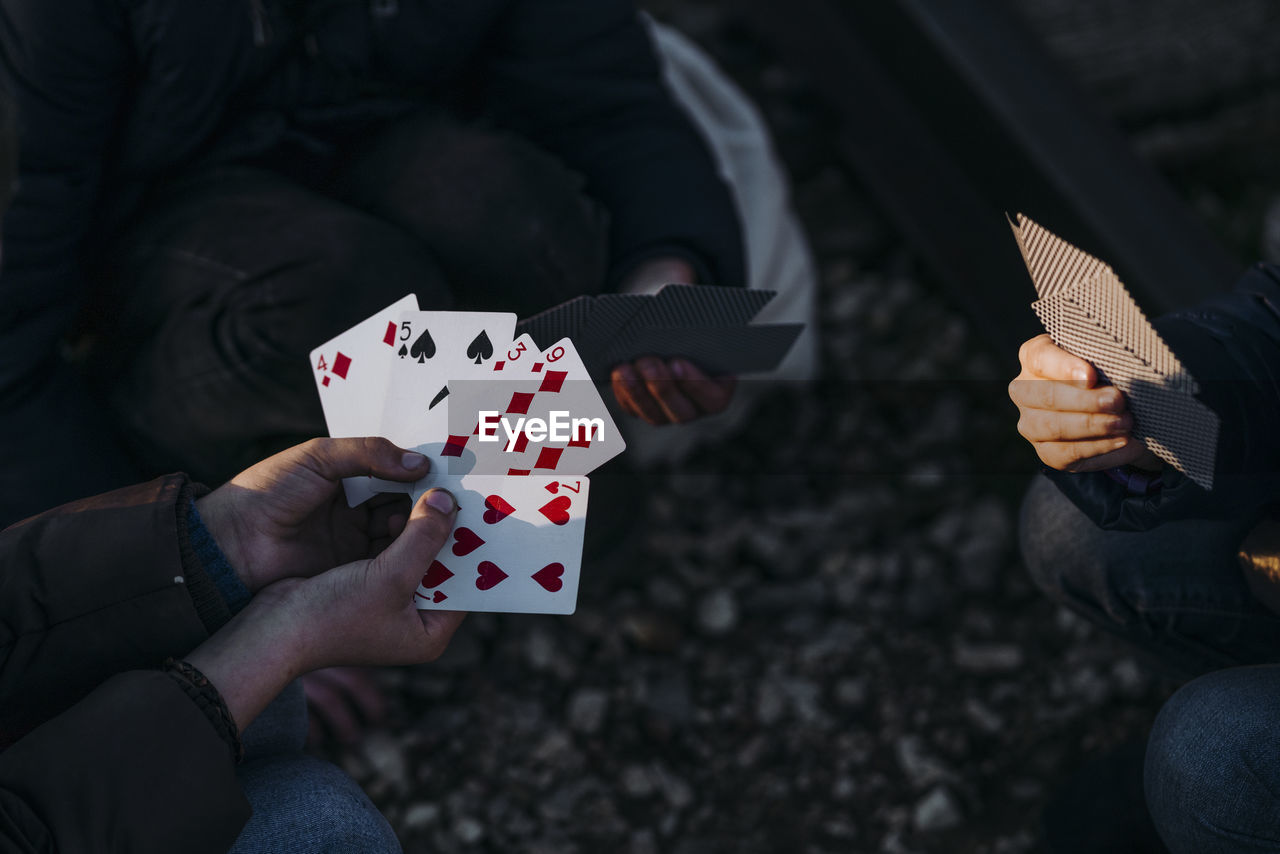 Crop hands of three children playing cards while sitting in a train track