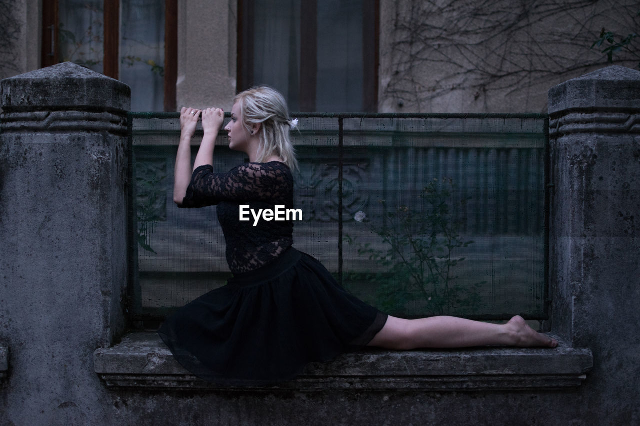 Full length of young woman sitting on gate