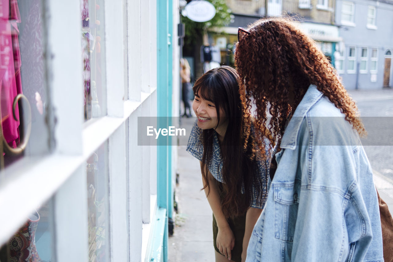 Happy friends window shopping together standing on footpath