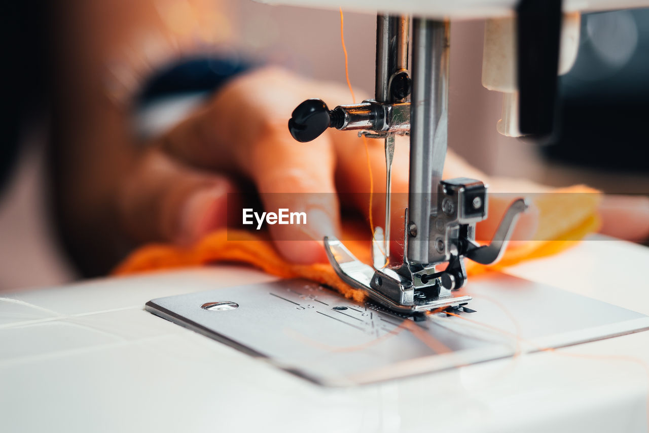 Cropped hand of woman using sewing machine at workshop