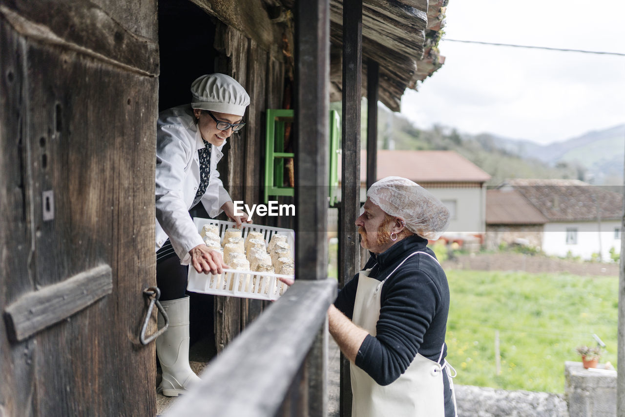 Smiling owner giving cheese tray to colleague at doorway