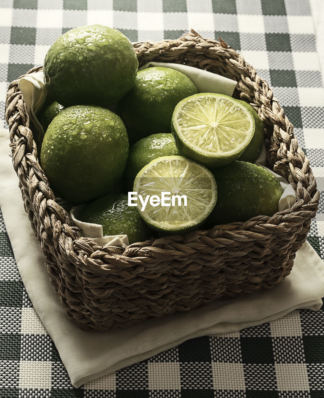 High angle view of wet limes in basket on tablecloth