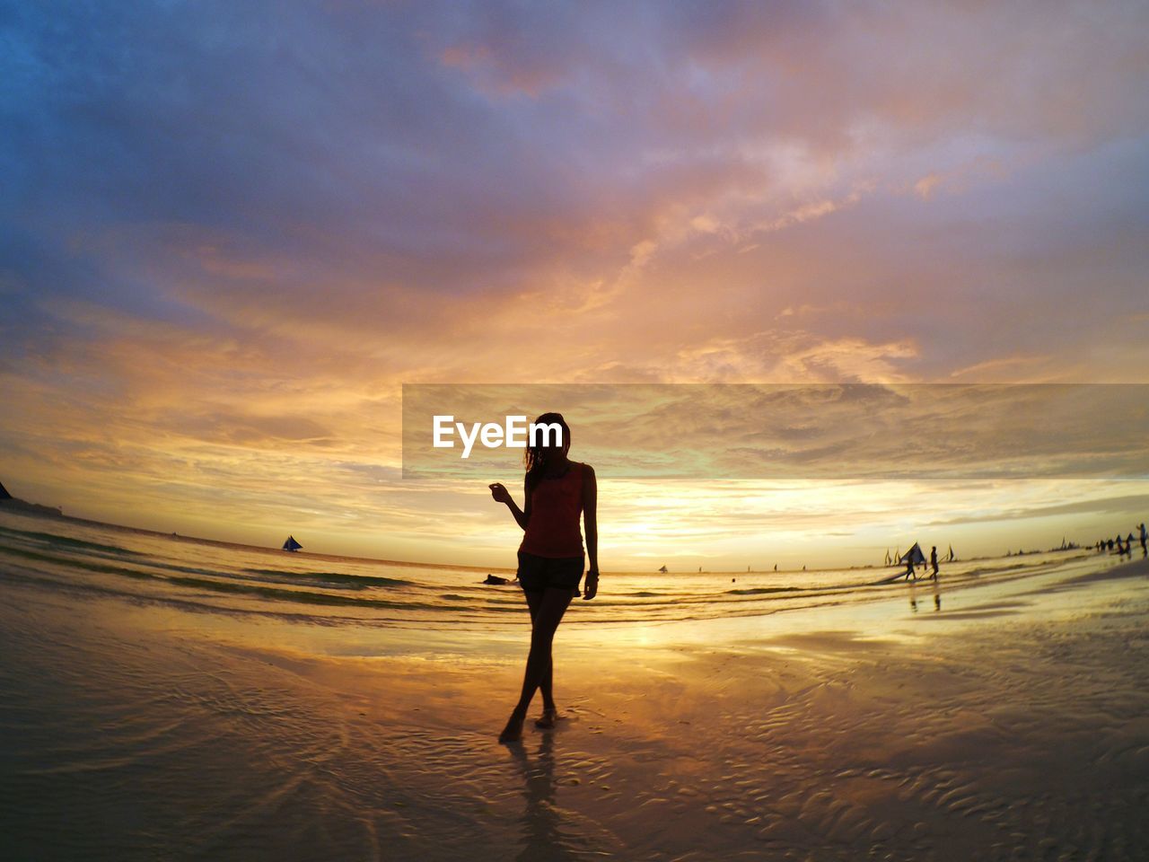 Silhouette woman standing on wet shore at beach against cloudy sky during sunset