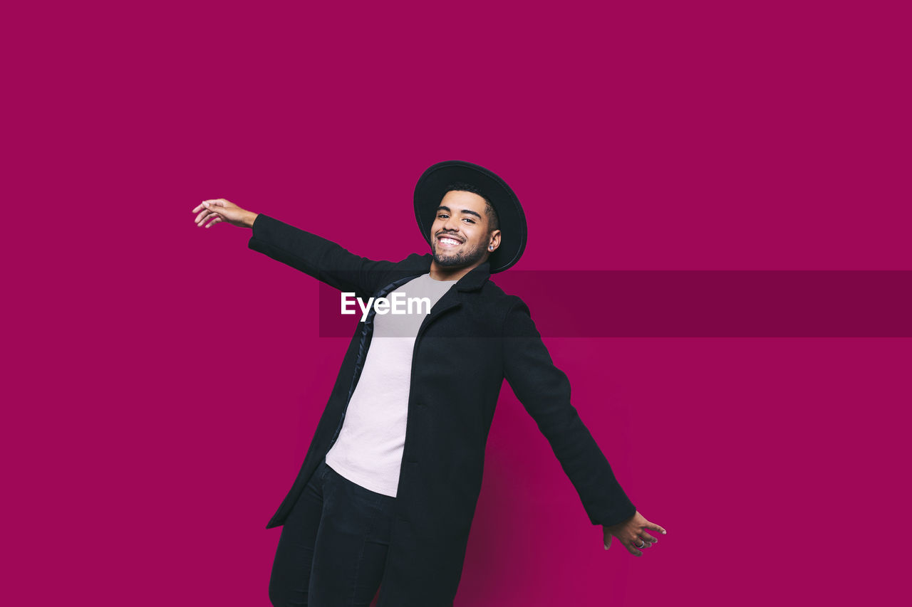 Smiling man with arms outstretched bending over backwards against pink background