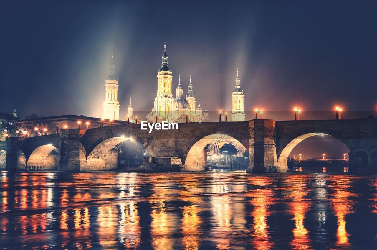Illuminated bridge against building in city at night