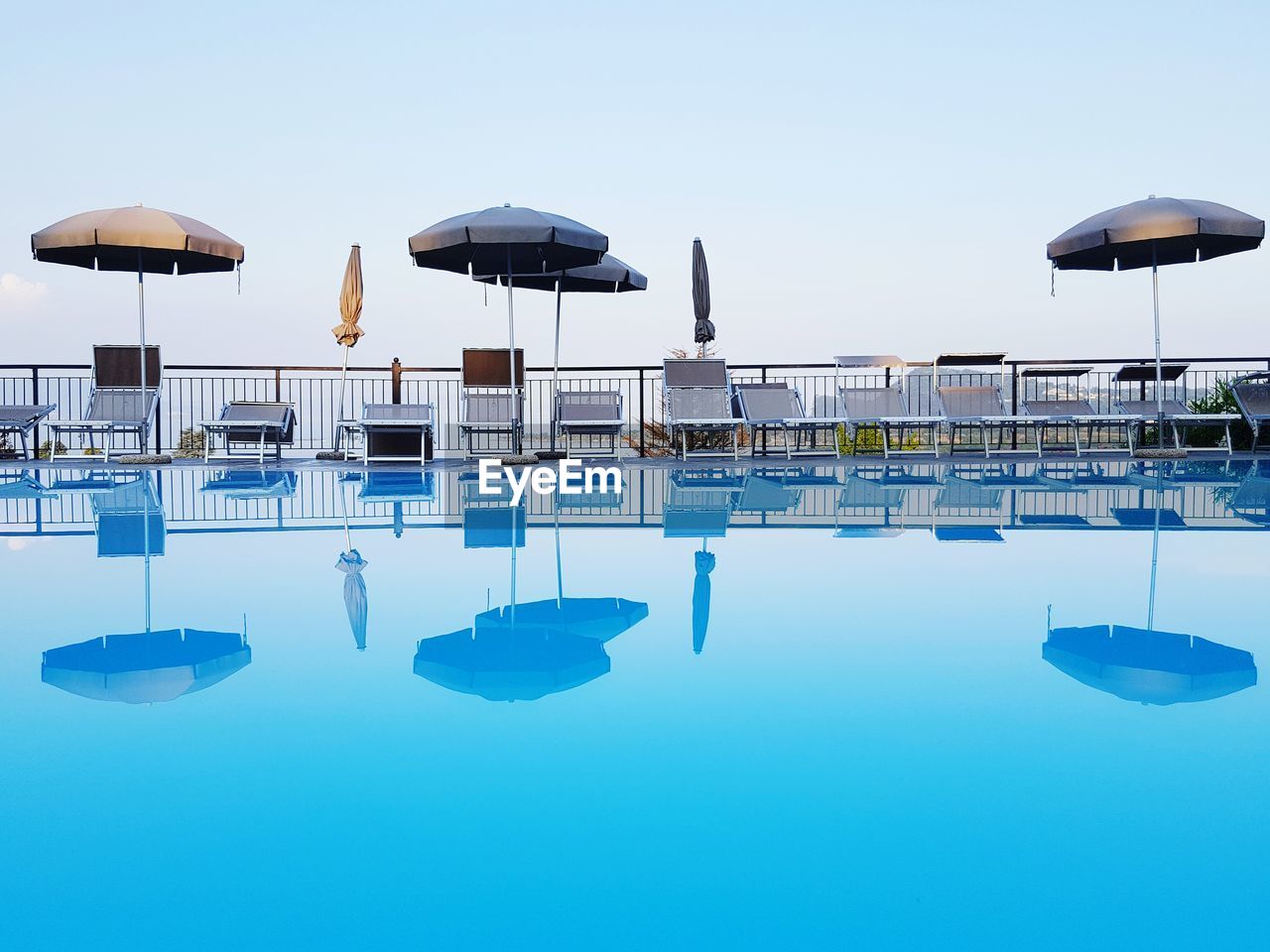 Reflection of umbrellas and lounge chairs in swimming pool against clear sky