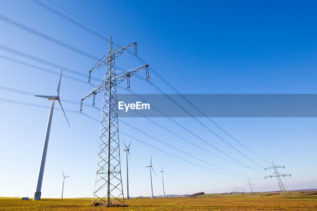 LOW ANGLE VIEW OF ELECTRICITY PYLONS ON FIELD AGAINST CLEAR BLUE SKY