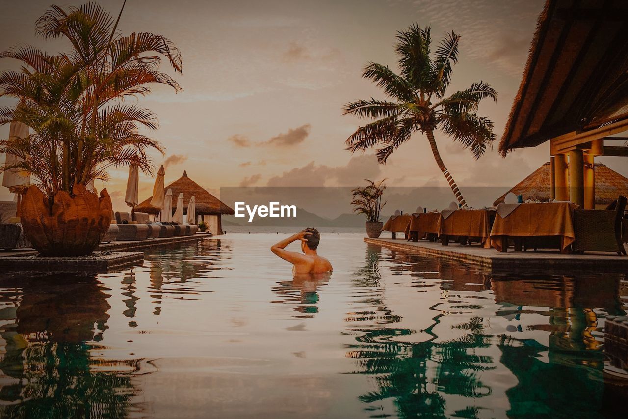 Man swimming in infinity pool against sky during sunset