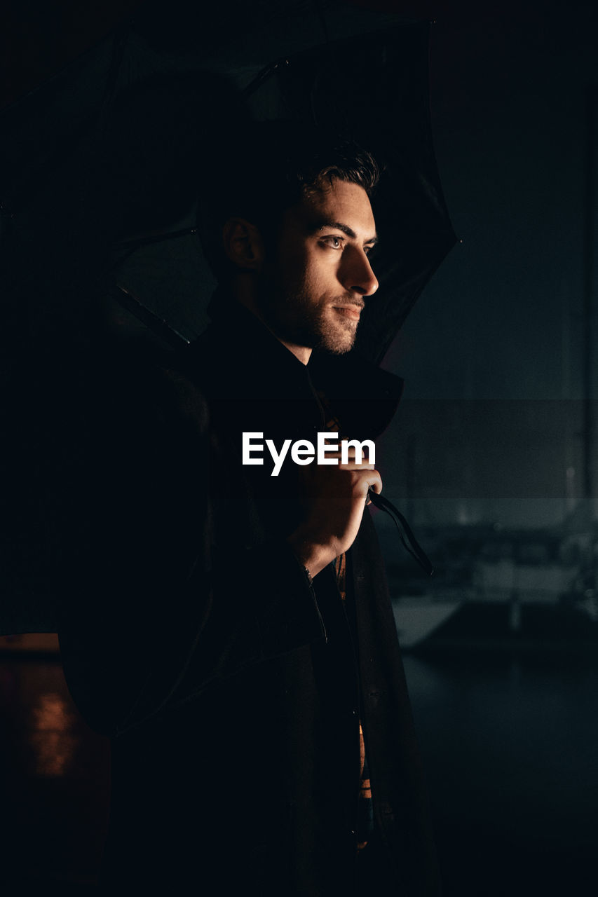 Young man looking away while standing outdoors at night