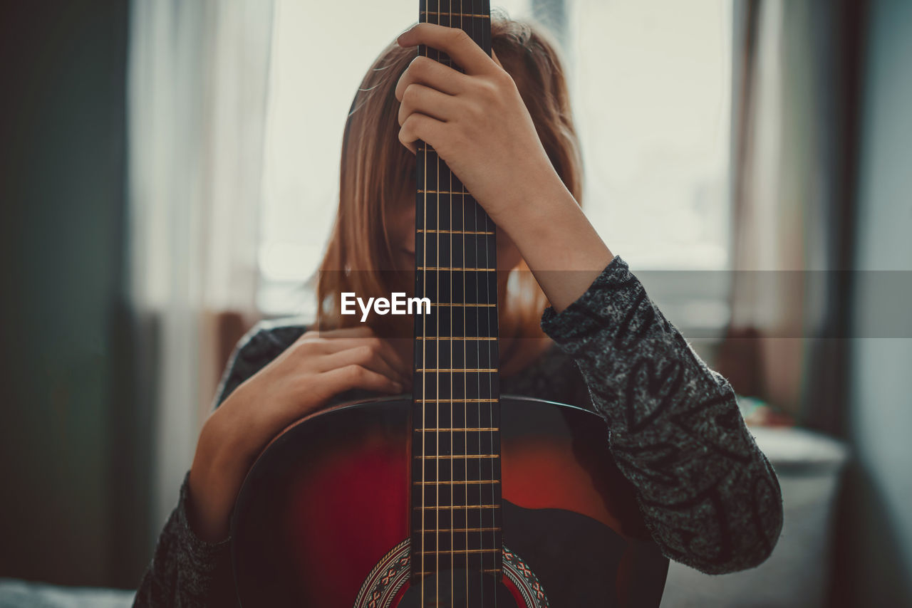 Woman hiding face with guitar at home