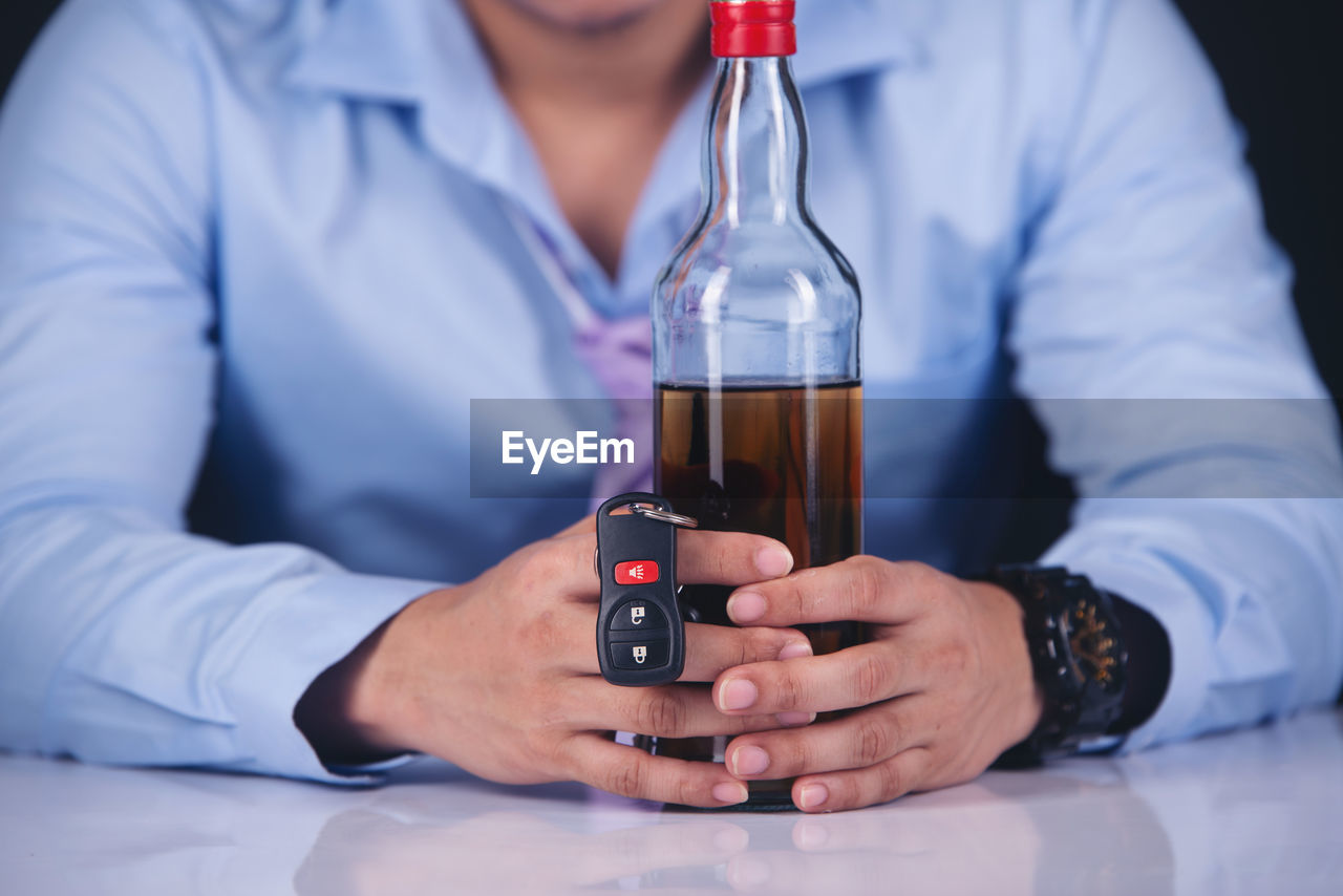 MIDSECTION OF MAN DRINKING GLASS ON TABLE AT HOME
