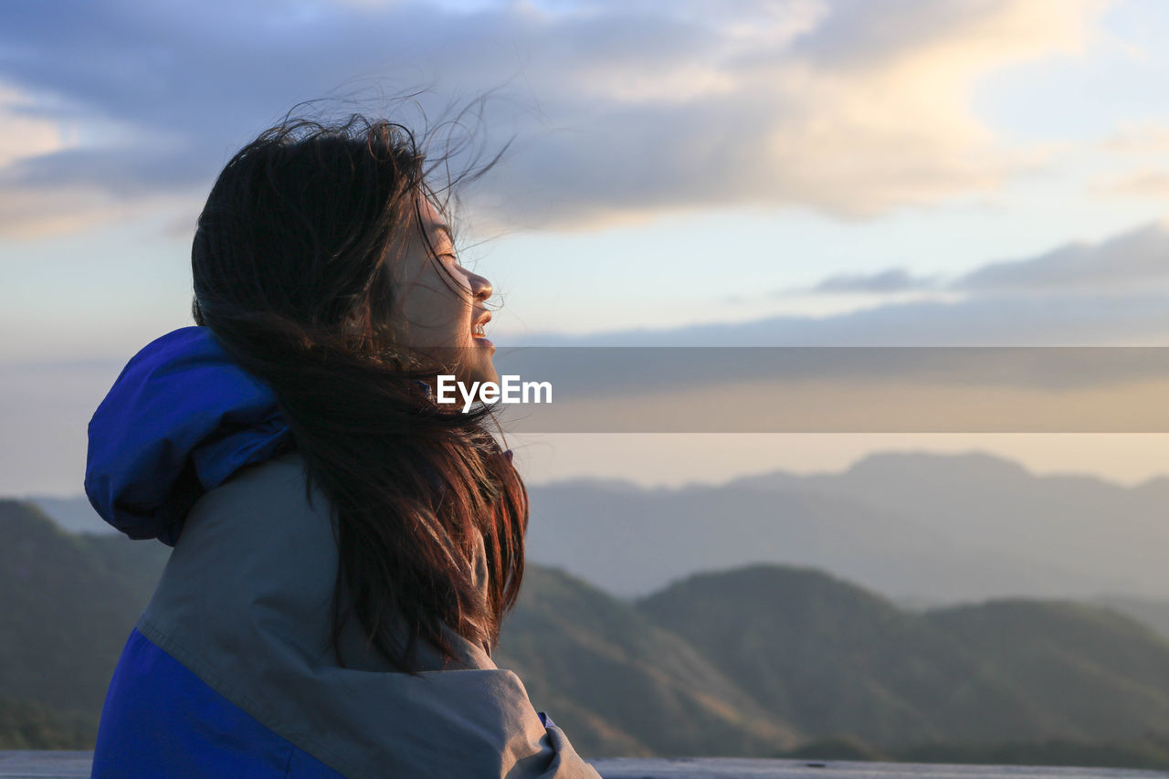 Side view of young woman against sky during sunset