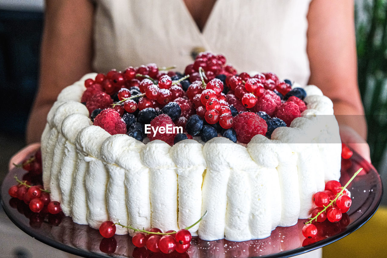 A woman is holding a beautiful cream cake with different types of berries