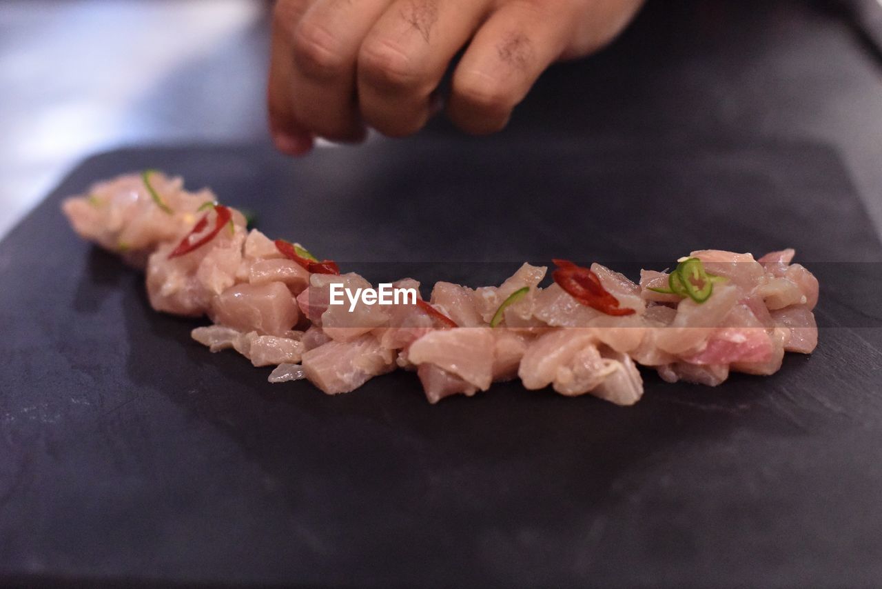 Cropped hand garnishing sushi on slate in kitchen