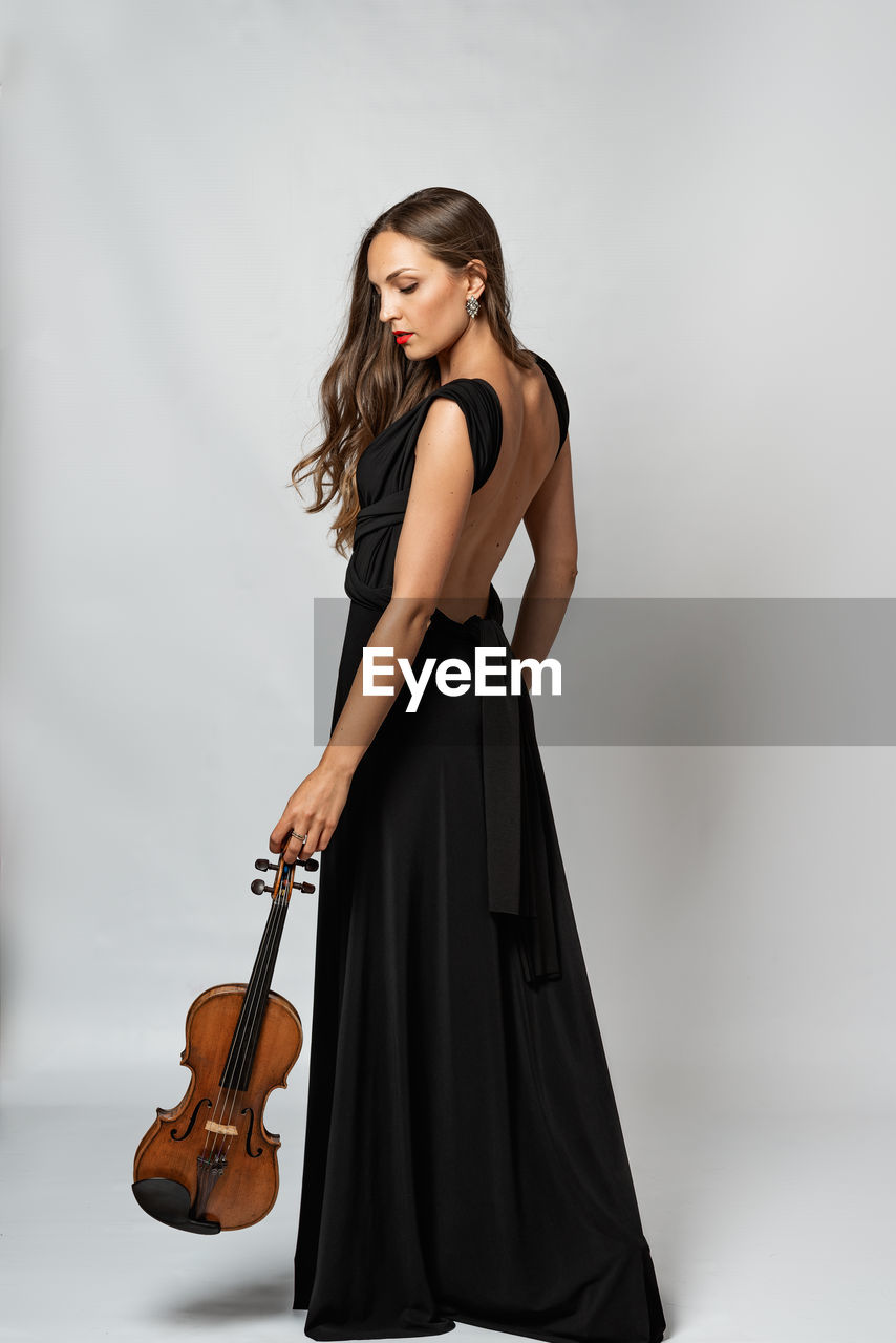 Side view of young woman holding violin standing against white background