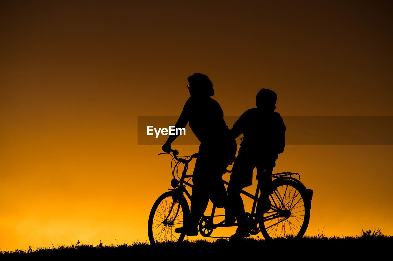 Silhouette of woman and her son riding bicycle