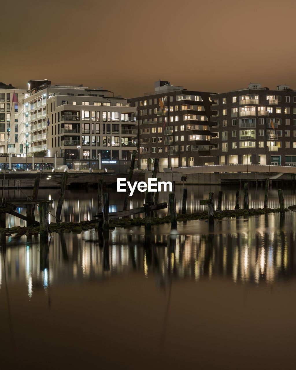 Illuminated buildings by river against sky at night