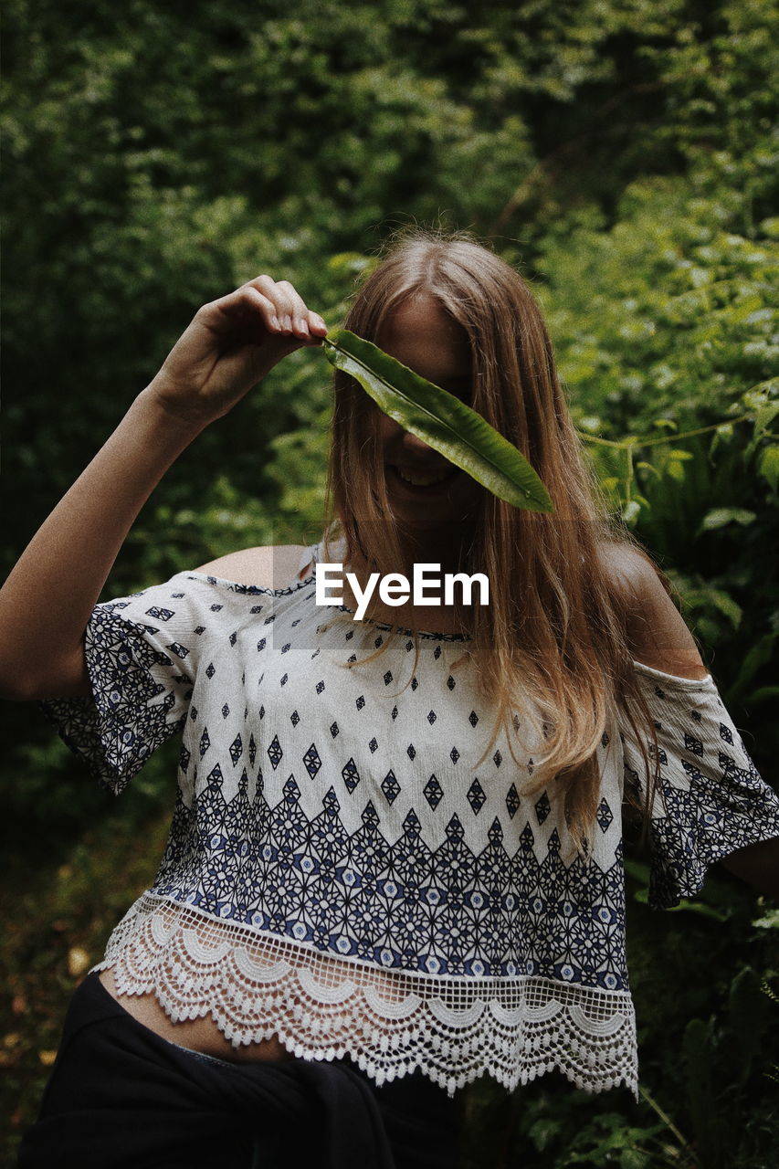 Teenage girl covering face with leaf while standing against plants
