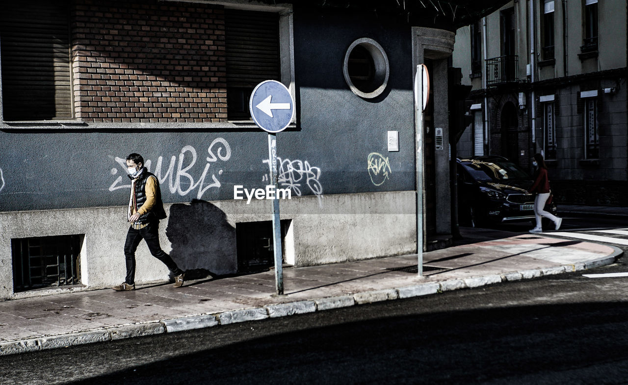 MAN ON FOOTPATH AGAINST GRAFFITI WALL