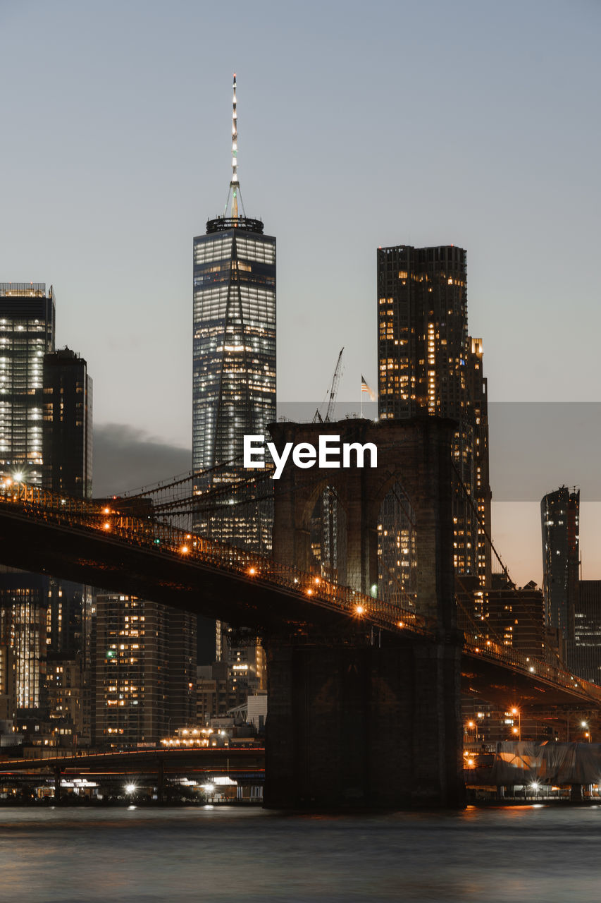 Low angle view of illuminated brooklyn bridge over river in city at dusk