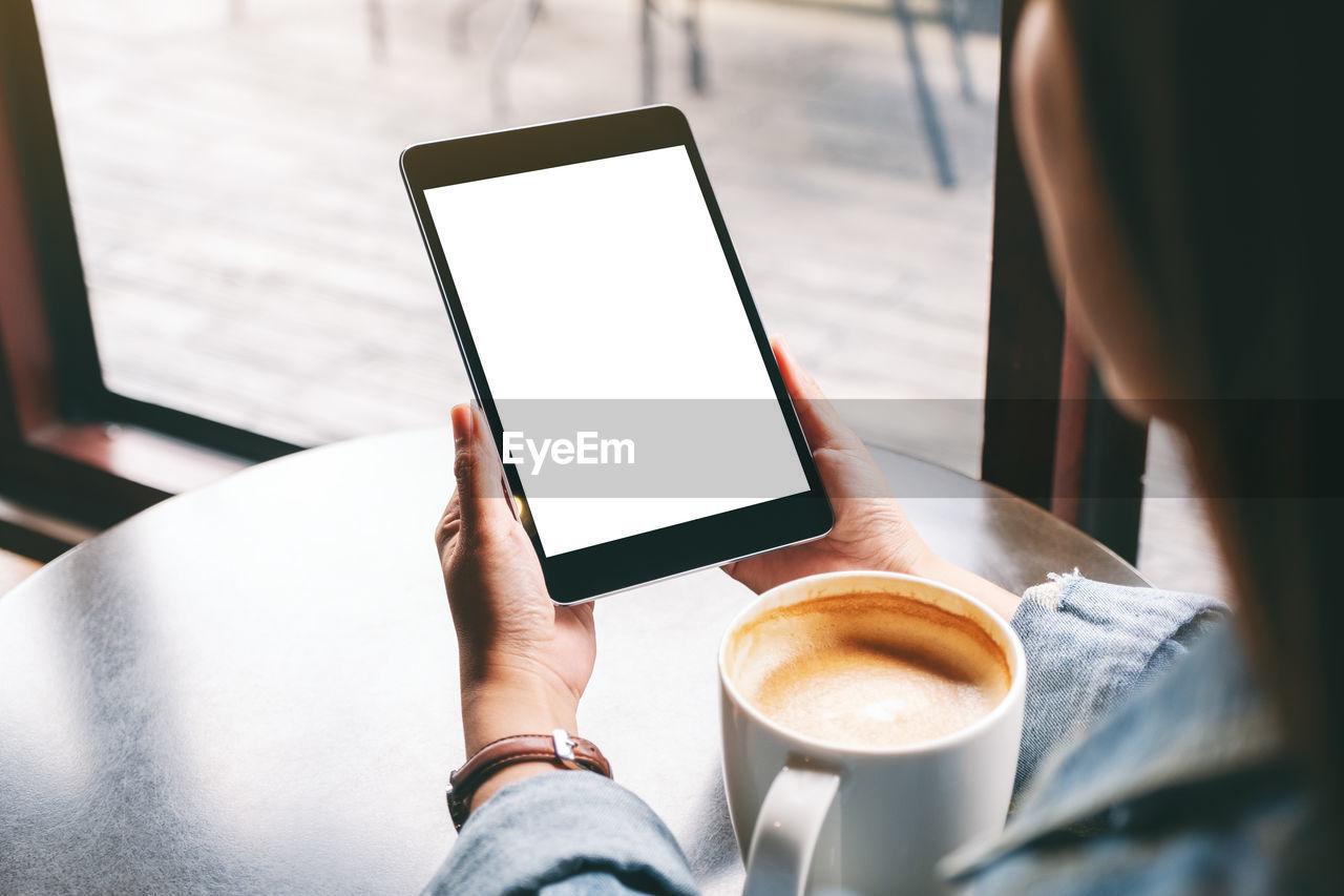 Cropped hand of woman holding digital tablet sitting at cafe