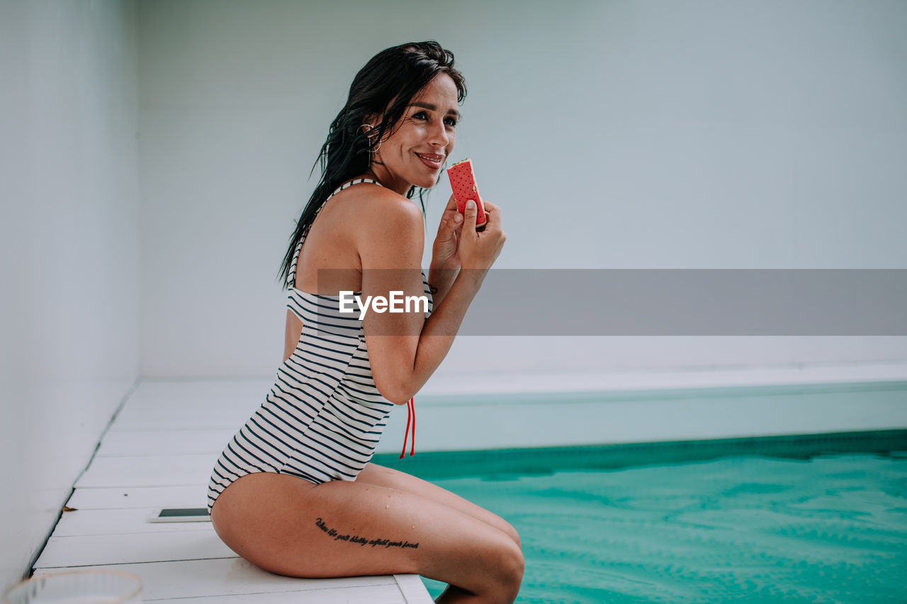 Young woman sitting in swimming pool against sea