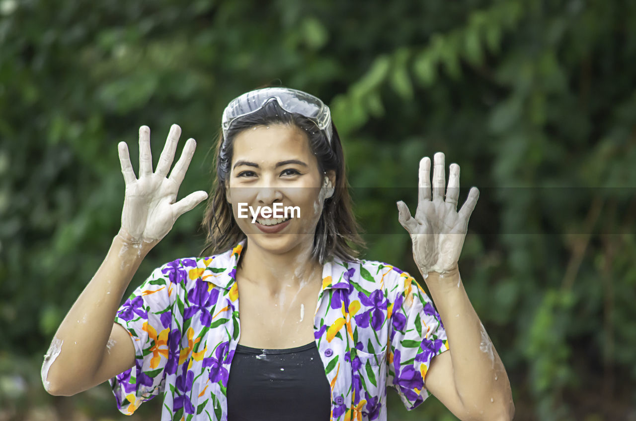 Portrait of smiling woman showing messy hands while standing against trees