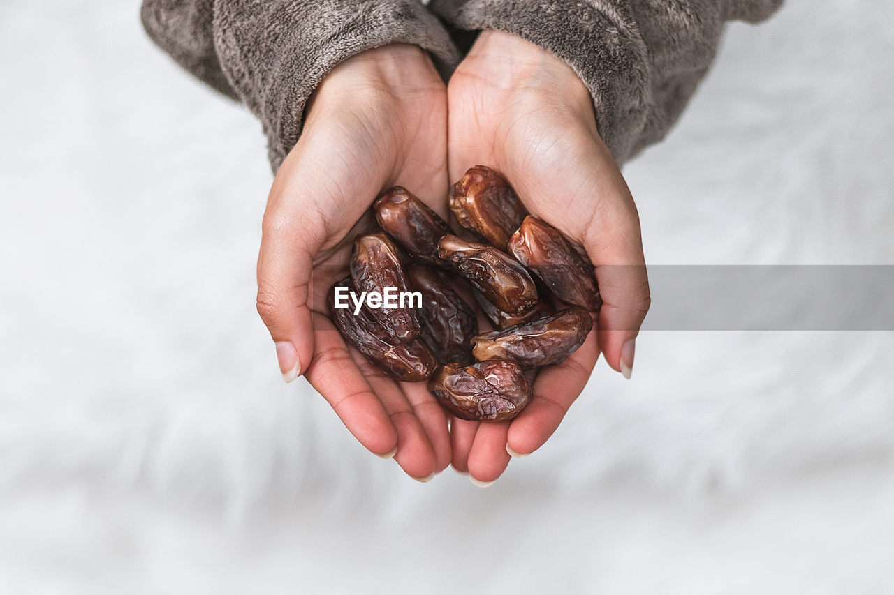 Close-up of female hands holding dates giving, sharing against blurred white background