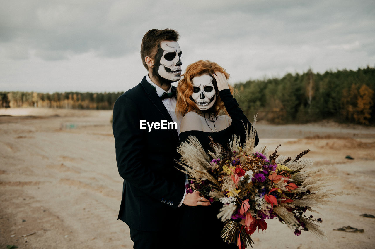 A couple in love celebrates halloween in costumes and makeup with a bouquet of dried flowers